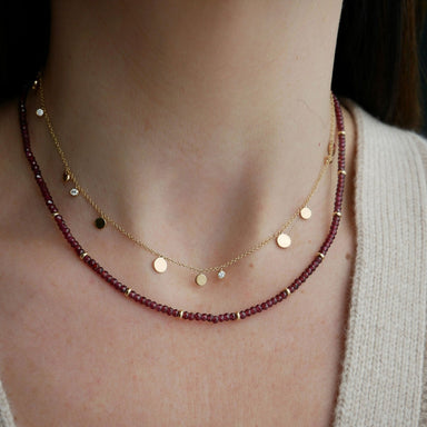 Birthstone Bead Necklace In Garnet styled on neck of model wearing diamond and gold confetti necklace and wearing tan sweater