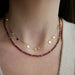 Birthstone Bead Necklace In Garnet styled on neck of model wearing diamond and gold confetti necklace and wearing tan sweater