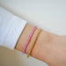 Birthstone Bead Bracelet in Pink Sapphire next to gold ball stretch bracelet styled on wrist of model wearing white sleeve