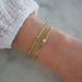 Birthstone Bead Bracelet In Peridot styled on wrist of model wearing diamond curb chain bracelet and white sleeve