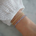 Birthstone Bead Bracelet In Tanzanite styled on wrist of model wearing gold ball bracelet and white sleeve