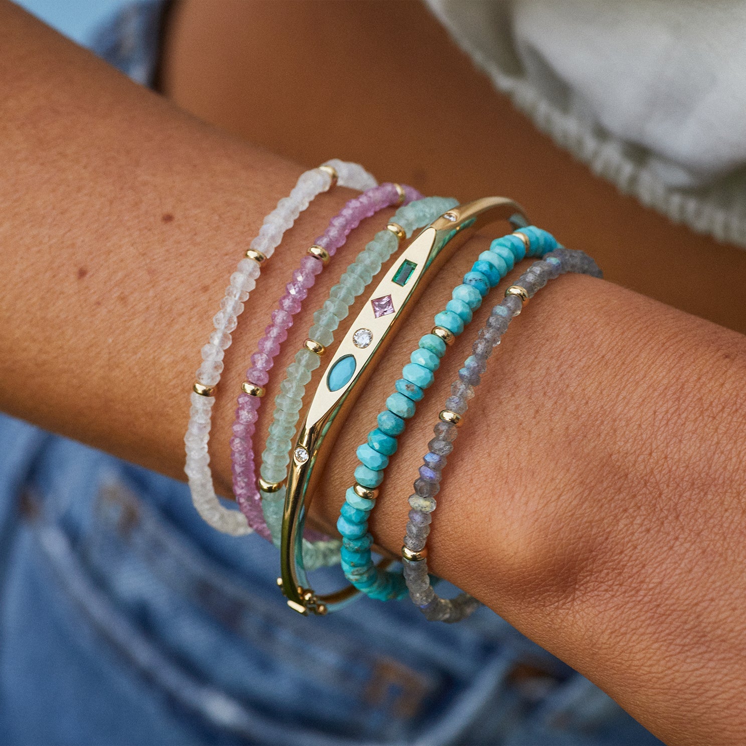 Birthstone Bead Bracelet In Moon Stone styled on wrist with four additional beaded bracelets with gold treasure bangle bracelet styled on wrist