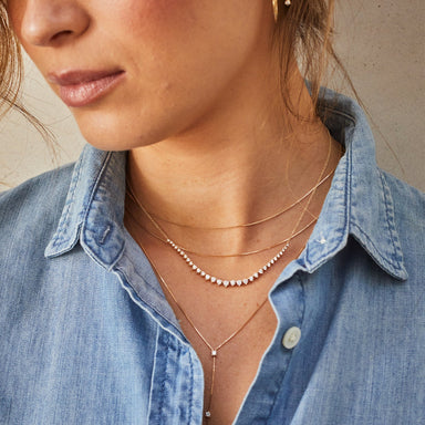 Graduated Diamond Necklace in 14k yellow gold styled on neck of model with two layered necklaces and wearing blue denim blouse
