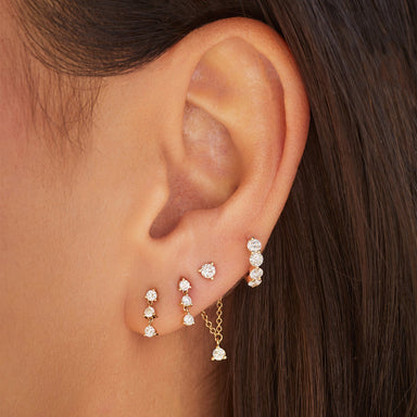 Triple Prong Set Diamond Stud Earring in 14k yellow gold featured in first and second earring hole next to diamond suspended earring and diamond jumbo huggie on ear of model
