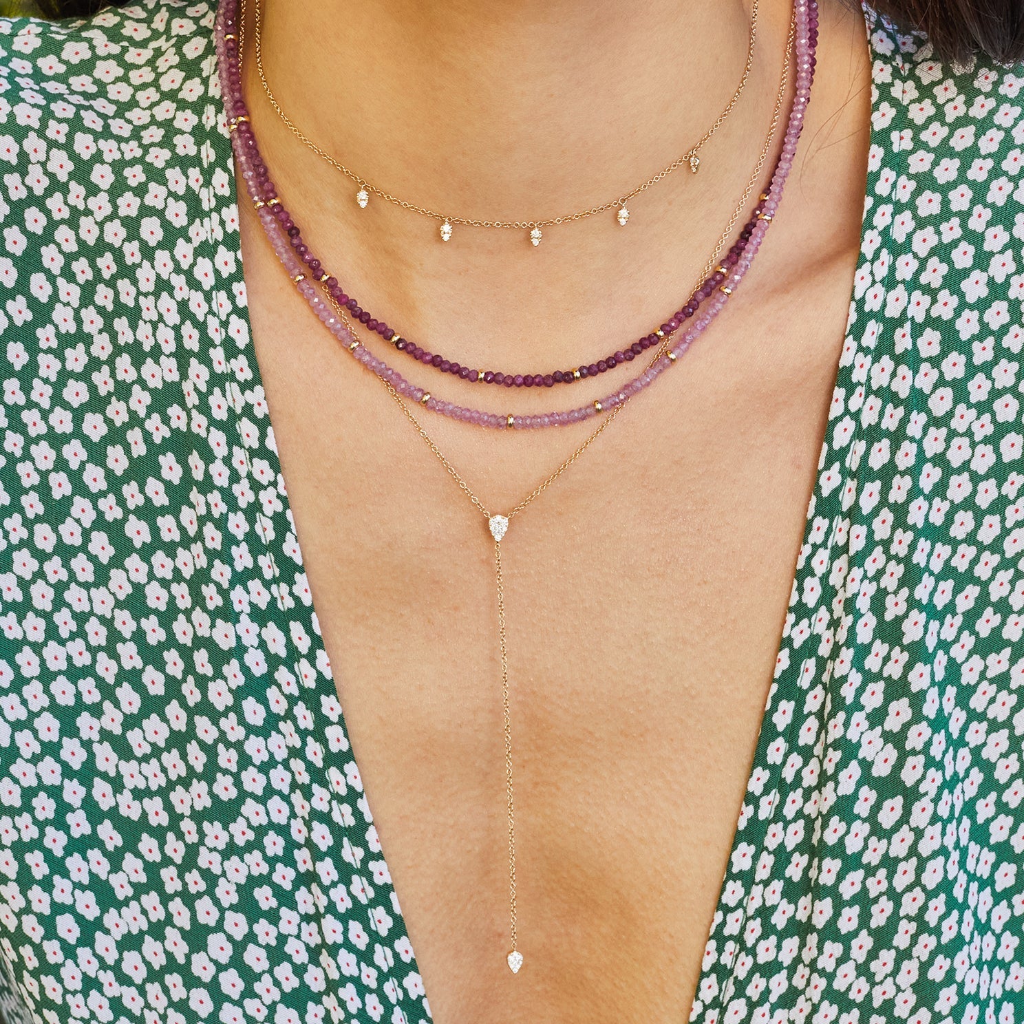 Full Cut Diamond Teardrop Lariat Necklace in 14k yellow gold styled on neck of model with gold and diamond necklace and two beaded necklaces. Model in green and white top